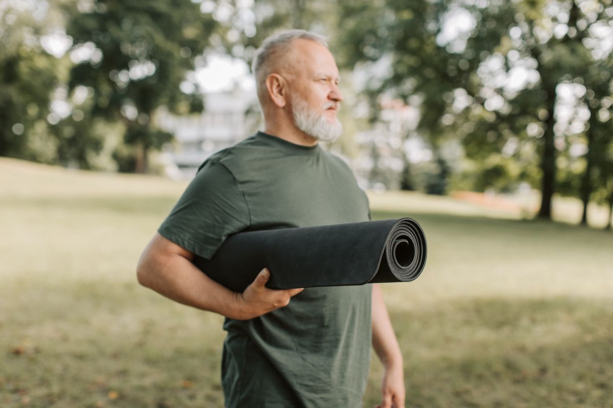 Man i femtioårsåldern med en yogamatta under armen i en park
