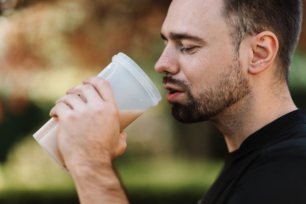 Man med skägg som dricker en smoothie ur en mugg utomhus