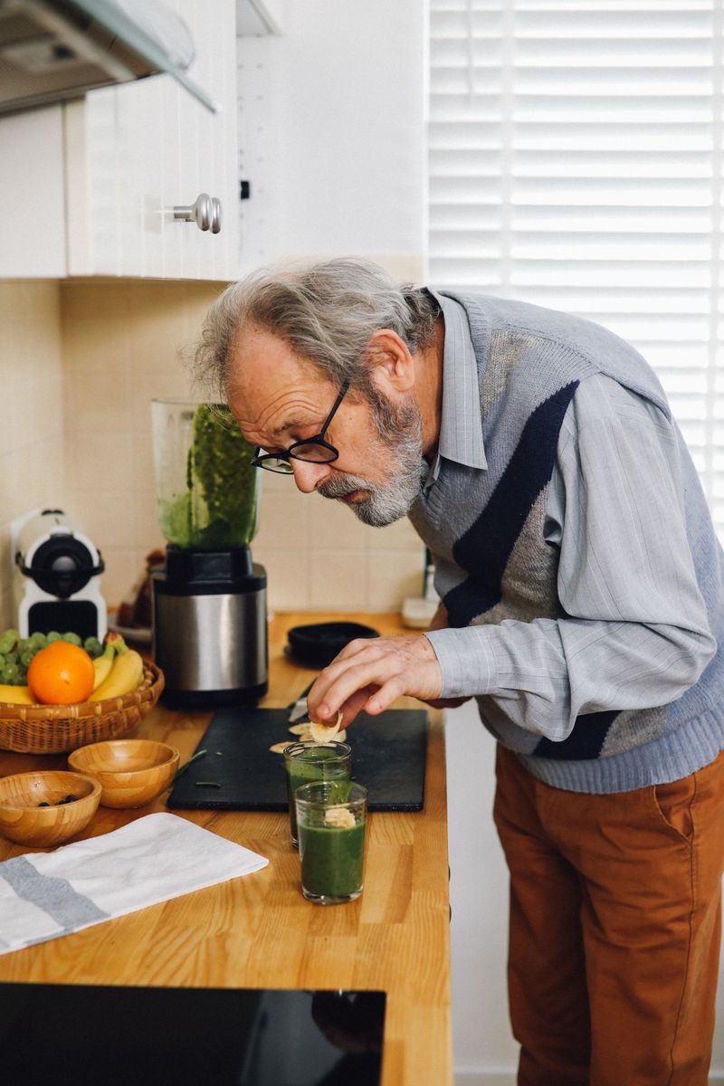 Äldre man som gör en grön smoothie i sitt kök