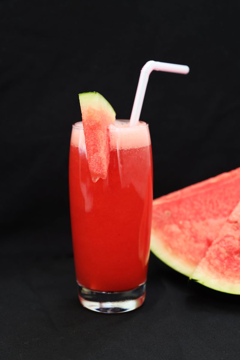 Glas vattenmelonsaft med sugrör bredvid en skiva vattenmelon